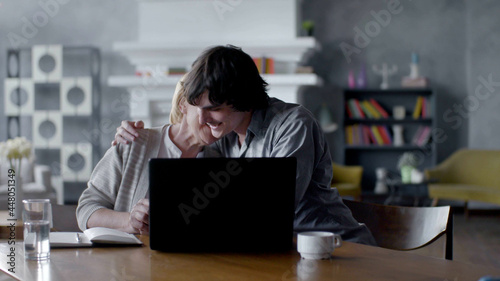 Adult grandson teaching elderly grandmother to use laptop and hugging