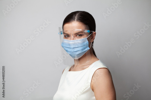 Woman physician in face shield looking at camera. Portrait of female doctor or nurse in medical mask and goggles on white background © millaf