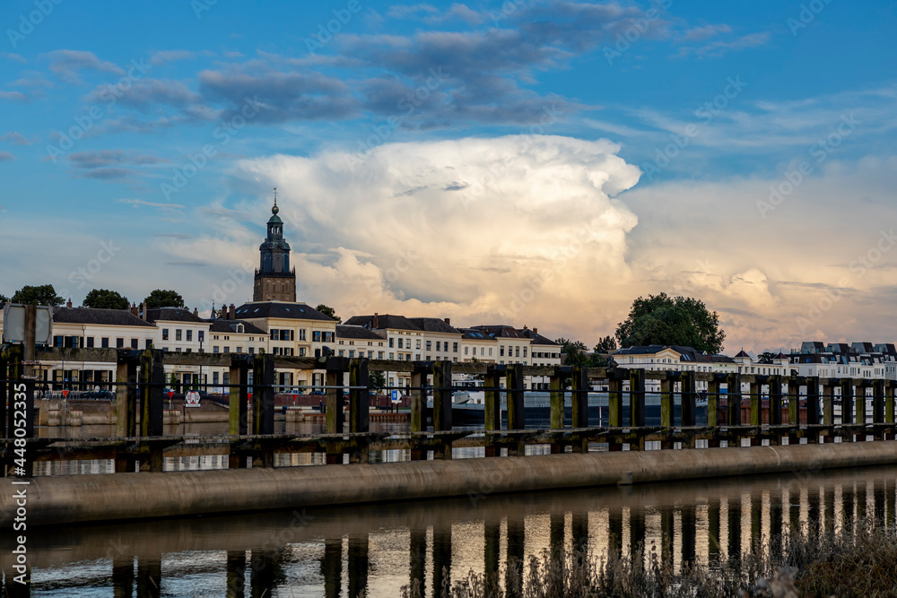 Wooden waterway passage with cityscape of Zutphen in The Netherlands behind and large cumulonimbus rain cloud rising above. Dutch climate and weather condition landscape.