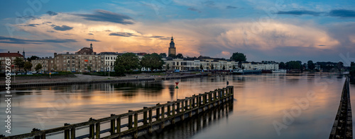 Colorful dramatic cityscape panorama of Zutphen in The Netherlands with large cumulonimbus rain clouds above reflecting in the river IJssel in the foreground. Dutch weather condition landscape.