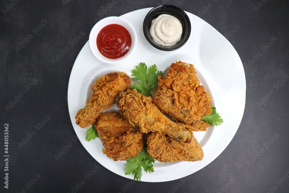 Fresh, hot, crispy deep fried chicken served on a white plate with tomato ketchup and mayonnaise. Chicken snack, hot fried chicken wings. Fast food over moody dark black background with copy space. Fresh, hot, crispy deep fried chicken served on a white plate with tomato ketchup and mayonnaise. Chicken snack, hot fried chicken wings. Fast food over moody dark black background with copy space.
