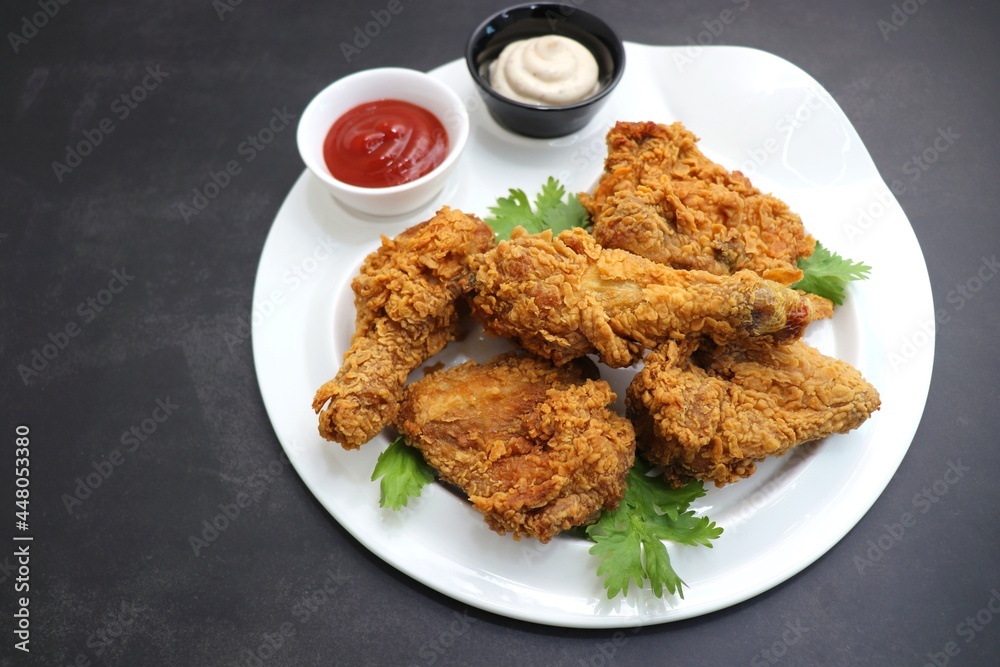 Fresh, hot, crispy deep fried chicken served on a white plate with tomato ketchup and mayonnaise. Chicken snack, hot fried chicken wings. Fast food over moody dark black background with copy space. Fresh, hot, crispy deep fried chicken served on a white plate with tomato ketchup and mayonnaise. Chicken snack, hot fried chicken wings. Fast food over moody dark black background with copy space.