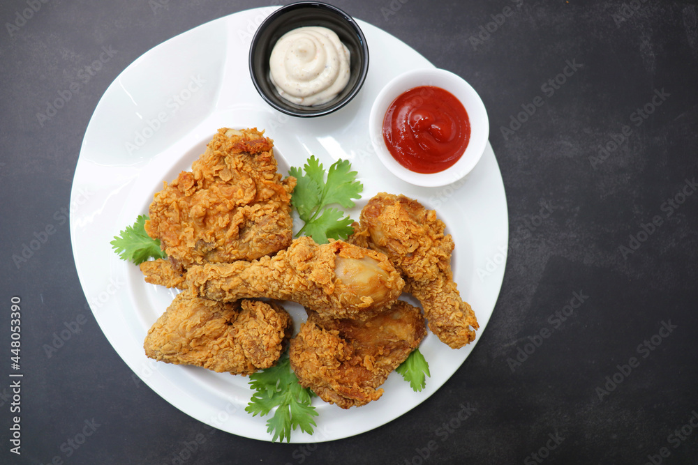 Fresh, hot, crispy deep fried chicken served on a white plate with tomato ketchup and mayonnaise. Chicken snack, hot fried chicken wings. Fast food over moody dark black background with copy space. Fresh, hot, crispy deep fried chicken served on a white plate with tomato ketchup and mayonnaise. Chicken snack, hot fried chicken wings. Fast food over moody dark black background with copy space.