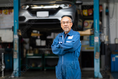 Portrait of a Asian senior mechanic working in his car service garage. Car maintenance and auto service garage concept.