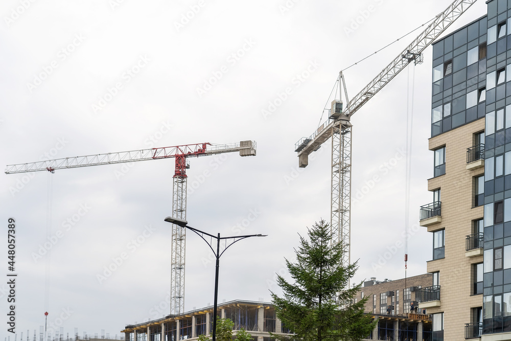 Finished residential building, unfinished residential buildings and construction cranes against clear blue sky. Housing construction site, apartment block with scaffolding Finished residential building, unfinished residential buildings and construction cranes against clear blue sky. Housing construction site, apartment block with scaffolding