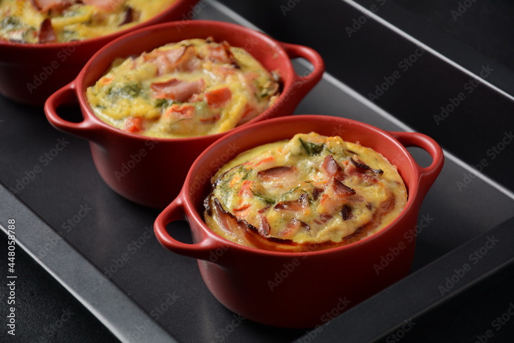 Omelette  with bacon, grated parmesan and greens in ceramic cocotte on oven tray. Tasty breakfast