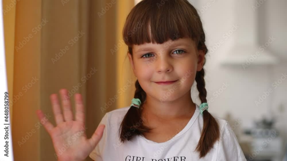 Cute dark haired girl with pigtails wearing white casual t shirt standing indoor and looking at camera with charming smile, waving hand, greeting or saying good bye. Cute dark haired girl with pigtails wearing white casual t shirt standing indoor and looking at camera with charming smile, waving hand, greeting or saying good bye.