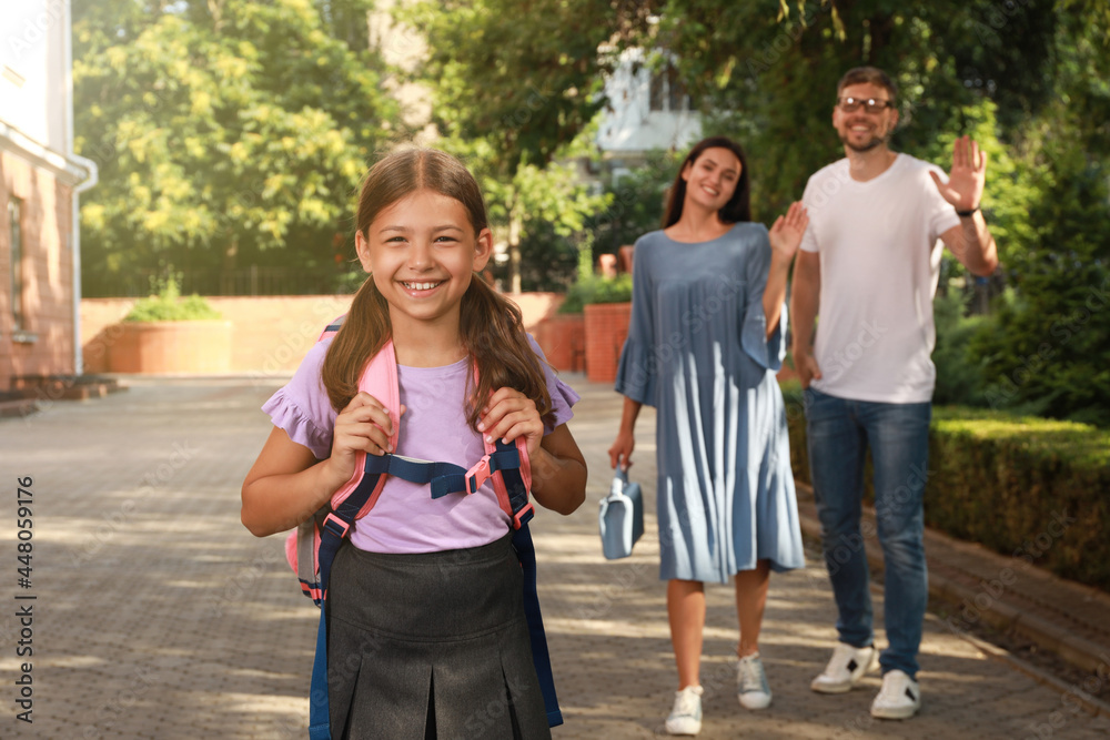 Obraz premium Parents waving goodbye to their daughter before school outdoors