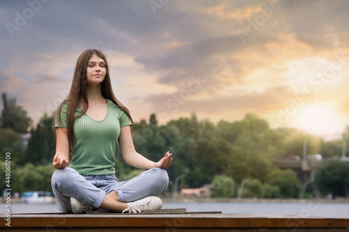 Teenage girl meditating near river. Space for text