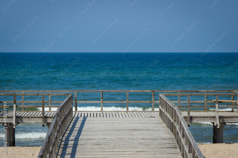 Wooden empty jetty or pier and beach by sunny sea. Travel, tourism and summer time