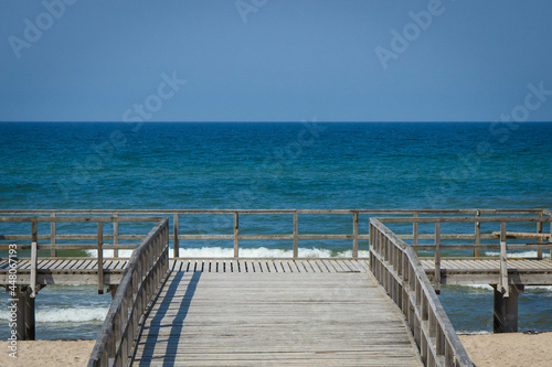 Wooden empty jetty or pier and beach by sunny sea. Travel, tourism and summer time