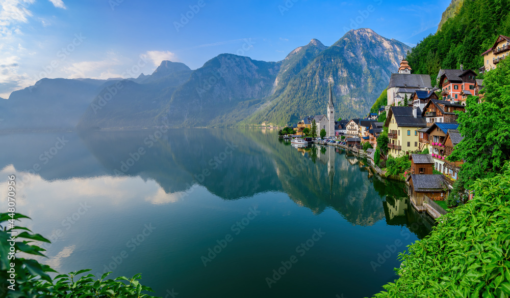 Hallstatt, Austria ; July 31, 2021 - A scenic picture postcard view of the famous village of Hallstatt reflecting in Hallstattersee lake in the Austrian Alps.