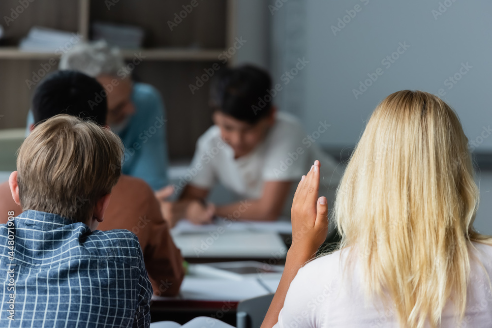 Schoolgirl raising hand near classmates in classroom Schoolgirl raising hand near classmates in classroom