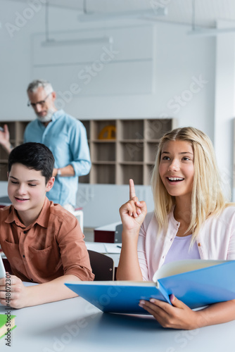 Smiling schoolkid having idea and holding book in classroom