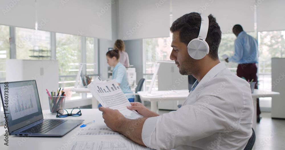 Joyful businessman wearing headphones having fun enjoying music sitting at desk in creative office. Joyful businessman wearing headphones having fun enjoying music sitting at desk in creative office.