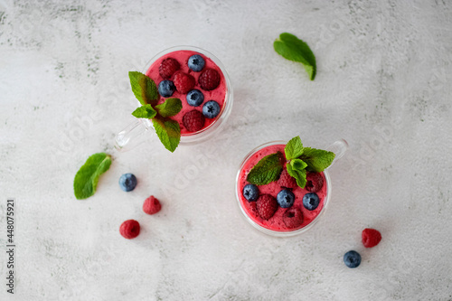 Berry smoothies in glass cups and blueberries and raspberries on a light background. Top view.