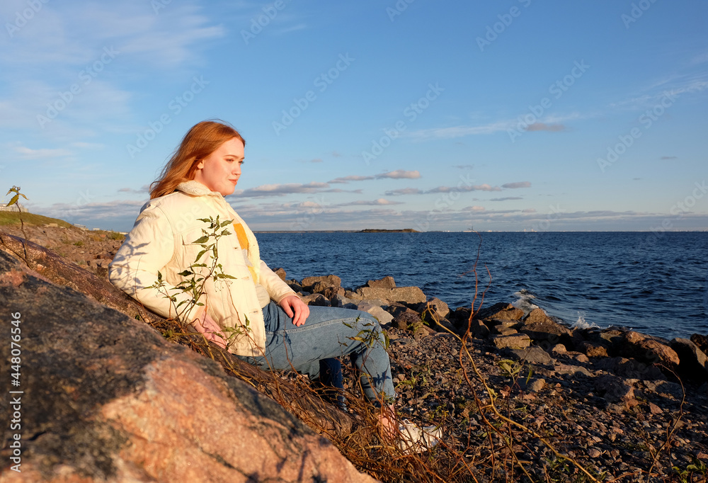 Beautiful girl body positive looking ahead on rocks seaside background in autumn season