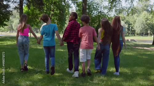 Rear view of diverse teen international friends hold hands walking in park