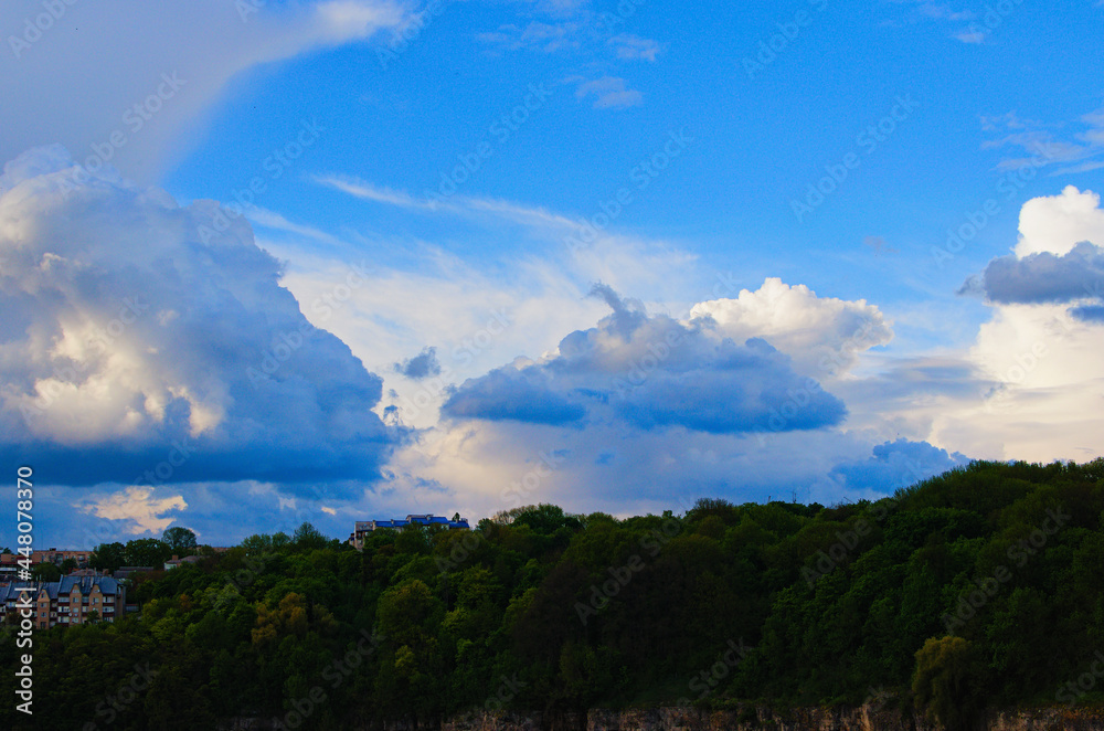 Colorful vibrant sky with white clouds over Smotrytsky canyon in Kamianets-Podilsky. Some modern residential buildings at the top of the canyon. Concept of landscape and nature