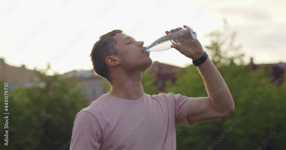 Medium shot of thirsty young man drinking water in plastic bottle outdoors. Medium shot of thirsty young man drinking water in plastic bottle outdoors.