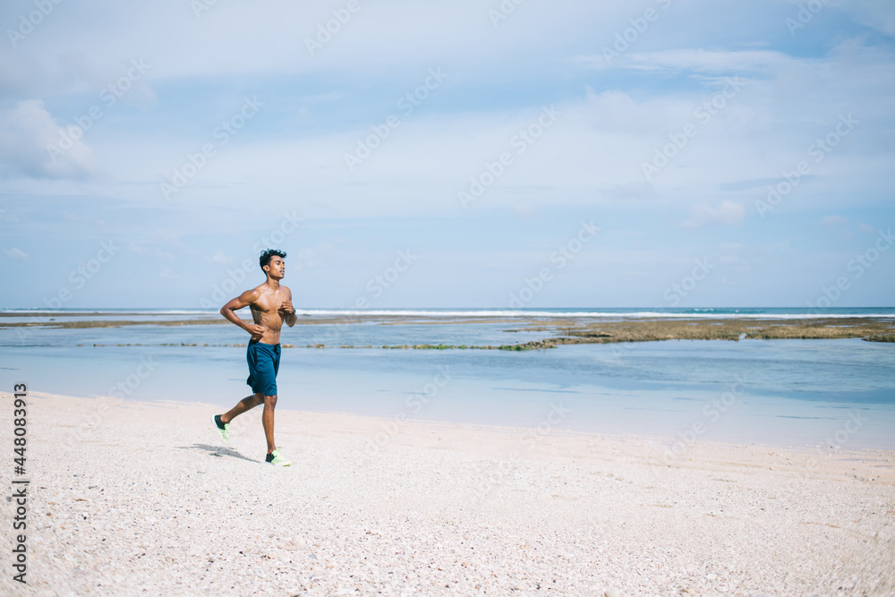 Adult ethnic sportsman running along sea beach Adult ethnic sportsman running along sea beach