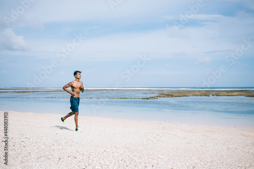 Adult ethnic sportsman running along sea beach © BullRun