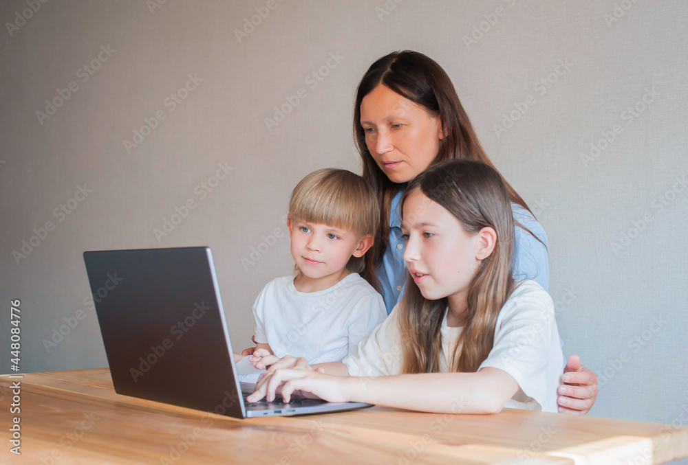 Mom with two children are sitting at home at the table with a laptop. Distance learning of children. Mom helps children learn remotely Mom with two children are sitting at home at the table with a laptop. Distance learning of children. Mom helps children learn remotely