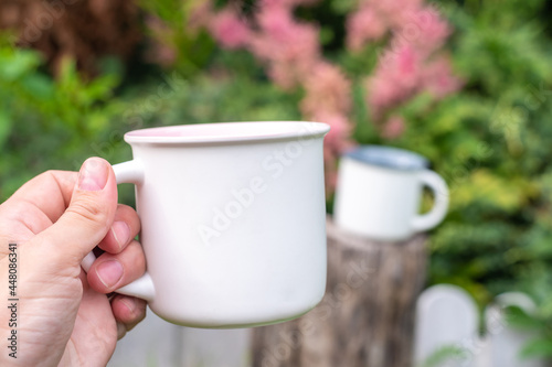 Mug mockup with bokeh green nature. Farmhouse rustic style. White mock up coffee cup in women hand. Blank mug printing design template.