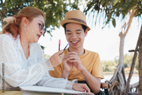 Asian Disabled child and Mother on wheelchair is playing  learning   drawing  reading in the outdoor city park like other people with family  Life in the education age  Happy disability kid concept