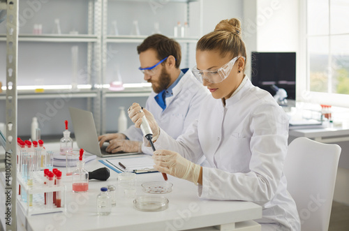 Female scientist making research in biochemical pharmaceutical lab analyzing new virus in blood. Young researcher taking sample with pipette. Vaccine coronavirus development concept. Selective focus