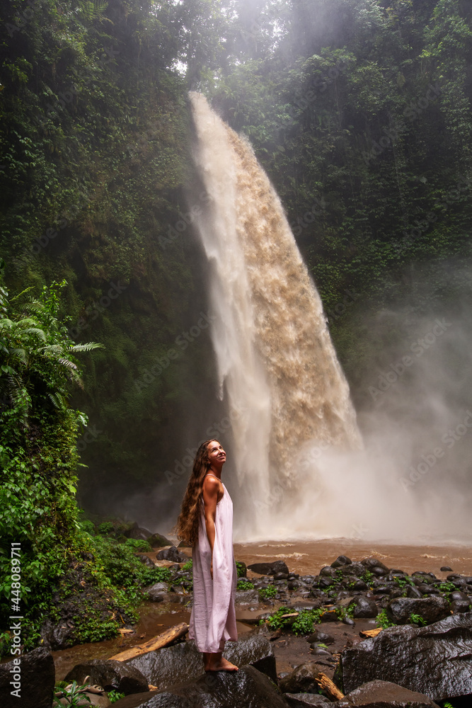 Naklejka premium Beautiful woman in a pink dress near a waterfall in Bali