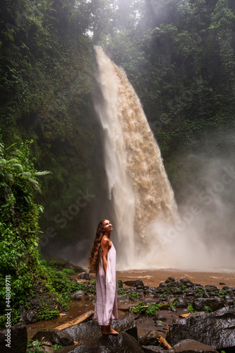 Beautiful woman in a pink dress near a waterfall in Bali