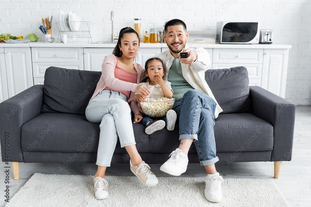 asian family watching tv and eating popcorn in living room