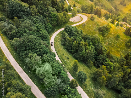 Aerial top down photo of a car driving on a beautiful snake serpentine road leading to mountain top in french Alps near Vaujany.