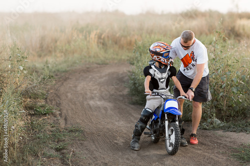 Kid on a motorcycle doing motocross. A little boy learns to ride a motorbike. The coach teaches the child to drive a motorcycle. Son and father on the track.