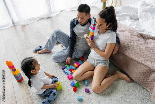 high angle view of asian husband and wife looking at toddler daughter playing building blocks