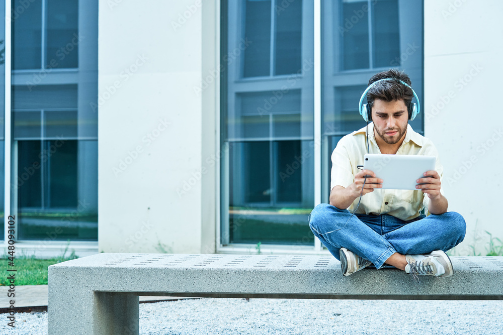 man sitting on a bench listening to music with headphones and his tablet
