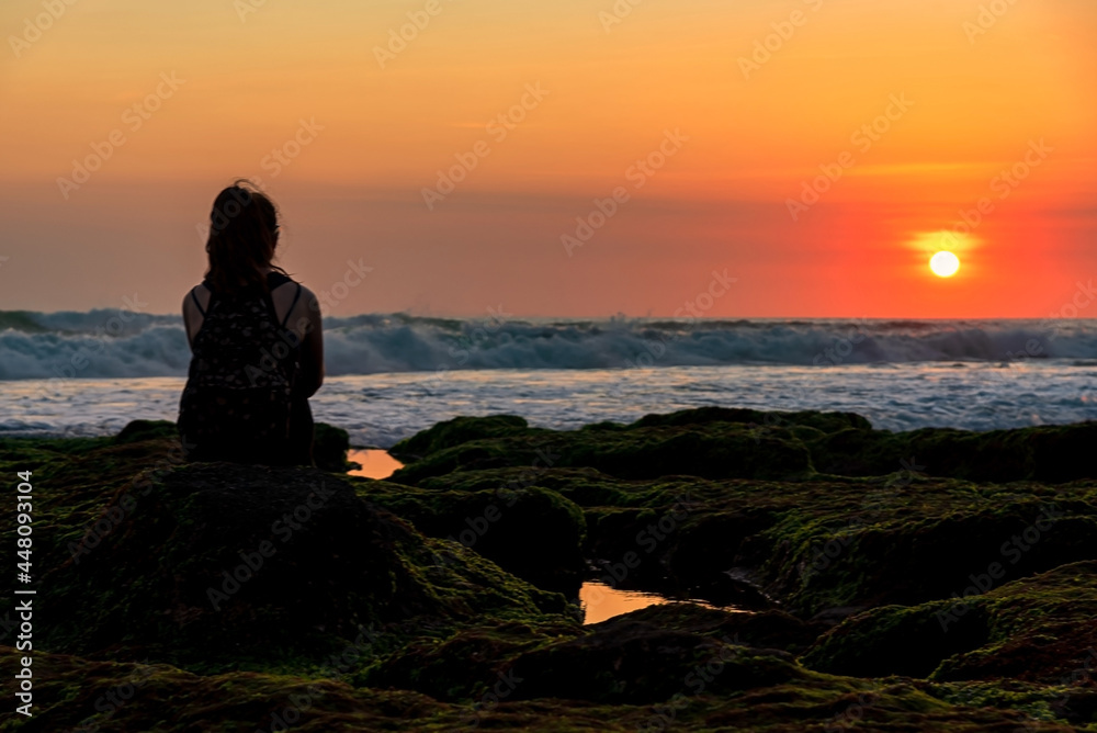 Silhouette of tourist sitting on a rock looking view the sunset over the sea in Bali, Indonesia.