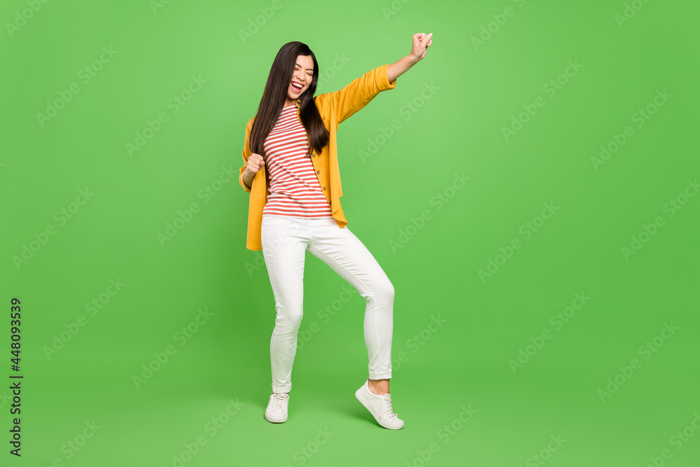 Full length photo of joyful brown hairdo young lady hands fists wear yellow shirt trousers isolated on green color background Full length photo of joyful brown hairdo young lady hands fists wear yellow shirt trousers isolated on green color background