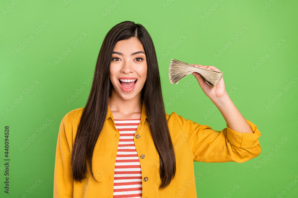 Photo of sweet impressed young woman dressed casual clothes holding money stack isolated green color background Photo of sweet impressed young woman dressed casual clothes holding money stack isolated green color background