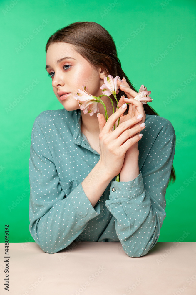 Crop female model with fresh flowers growing from blouse sleeves touching face against green background Crop female model with fresh flowers growing from blouse sleeves touching face against green background