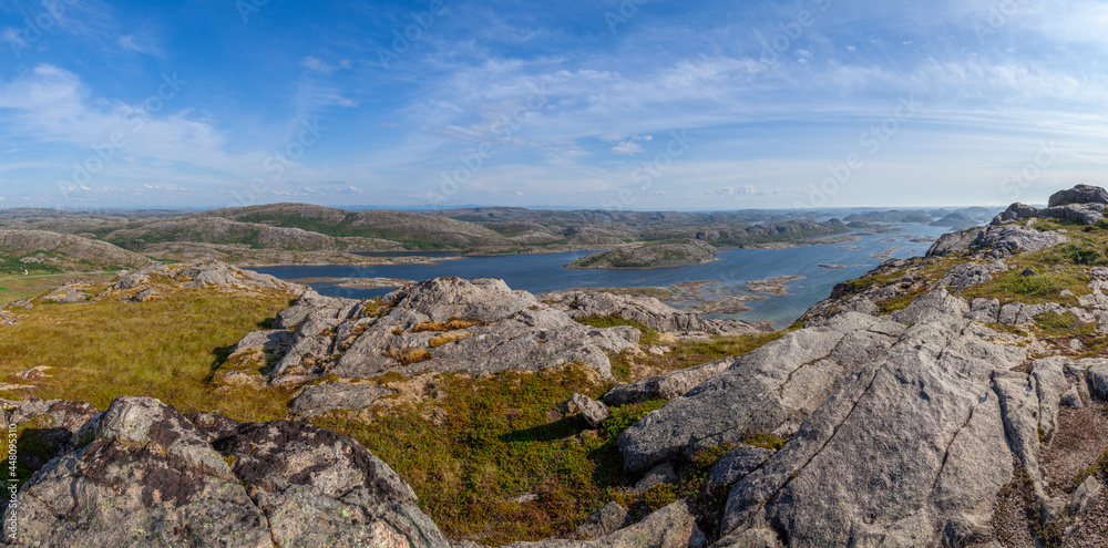 Wide panorama view from above of a rock cliff and the ocean and islands on the horizon under blue sky. Norway. Valoy. Vikna Islands in blue se