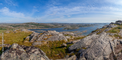 Wide panorama view from above of a rock cliff and the ocean and islands on the horizon under blue sky. Norway. Valoy. Vikna Islands in blue se