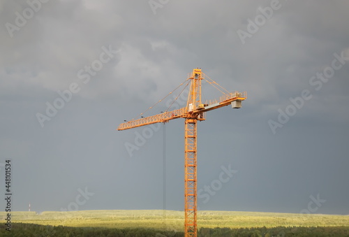 Yellow construction crane on the background of the sky and green fields.