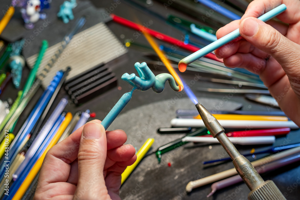 Hands of the glassmaker, making figurines from glass. Shaping hot murano glass into an elephant shape under a jet of fire from a gas burner. Handmade art. Selective focus. Close up. Hands of the glassmaker, making figurines from glass. Shaping hot murano glass into an elephant shape under a jet of fire from a gas burner. Handmade art. Selective focus. Close up.