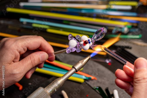 Hands of the glassmaker, making figurines from glass. Shaping hot murano glass into a bunny under a jet of fire from a gas burner.  Handmade fine art. Selective focus. Close up. photo