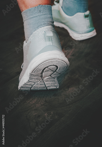 Sole of running shoe. Close up of female feet with snickers. against the background of a wooden floor photo