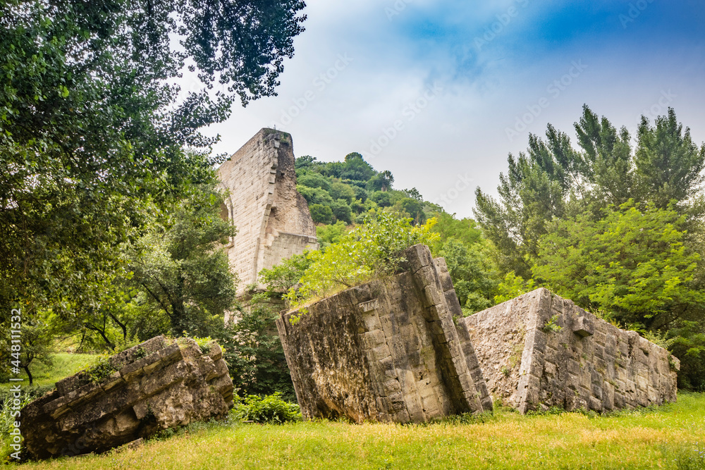 The ruins of the Roman arch bridge of Augustus, in Narni, Terni, Umbria. The remains of the bridge over the Nera river. The big and ancient stone arch, against the blue sky. Trees and dense vegetation