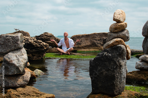 Adult slim man wearing white shirt exercising yoga or qigong on the sea or ocean shore on a nice summer day photo