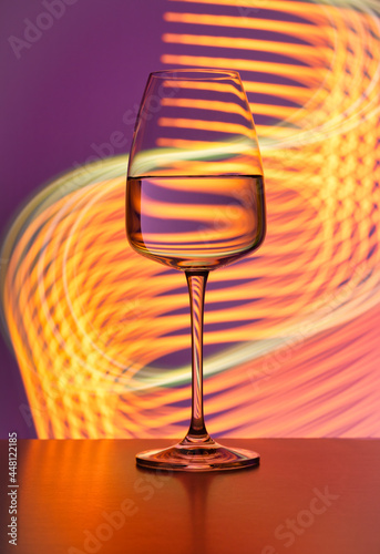 Crystal glass with pure water on a purple background painted with colorful light. No splashes, even surface. Light reflections and refractions, light streaks, party atmosphere, lifestyle, abstract.